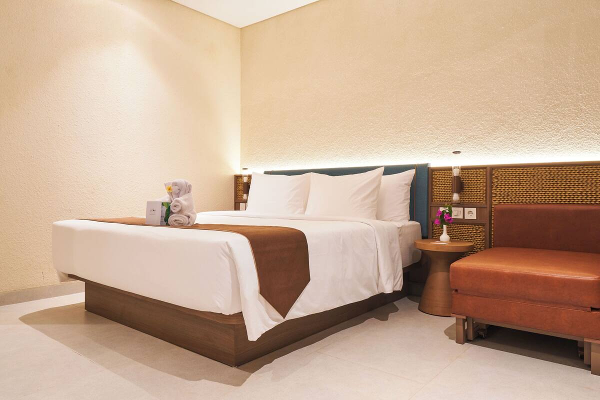 A hotel room with a bed, bedside table, and a small sofa.