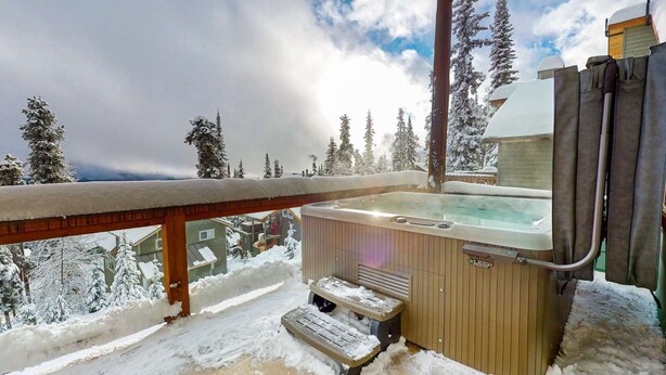 Ein Whirlpool mit Stufen, umgeben von schneebedeckten Bäumen und einer Holzterrasse.