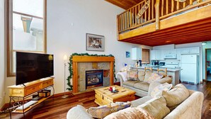 Ein Wohnzimmer mit Kamin, Fernseher, einer Couch und einer Küche im Hintergrund.