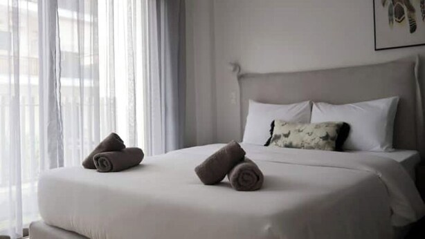 Una habitación de hotel con cama, almohadas y ventana con cortinas.