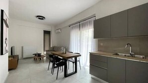 Una cocina moderna con armarios grises, una mesa de comedor de madera y una ventana con cortinas translúcidas.