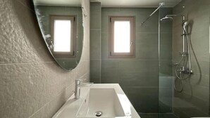 Un baño con un espejo grande, una bañera, una ducha y dos ventanas.