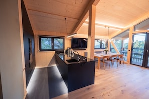 A modern kitchen with a black island, wooden beams, and a large window. - Superior Chalet mit Sauna & Hot Tub (Turrach)