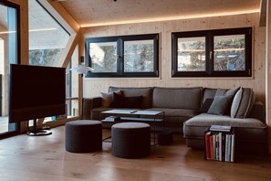 A modern living room with a sofa, ottomans, a coffee table, and a TV. - Premium Chalet with Sauna & Hot Tub (Turrach)