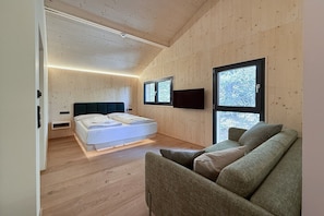 A modern bedroom with a bed, a sofa, wooden walls, and large windows. - Premium Chalet with Sauna & Hot Tub (Turrach)