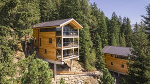 A wooden cabin with a glass balcony, surrounded by dense forest. - Deluxe chalet with sauna & hot tub (Turrach)