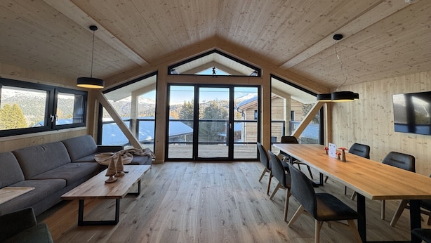 Una habitación amplia con techo alto, una mesa de comedor de madera, un sofá y ventanas grandes que ofrecen vistas al exterior.