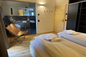 A modern hotel room with two beds, a wooden floor, a glass partition, a chair, and a bathroom visible through the glass. - Superior Chalet with Sauna & Hot Tub (Turrach)