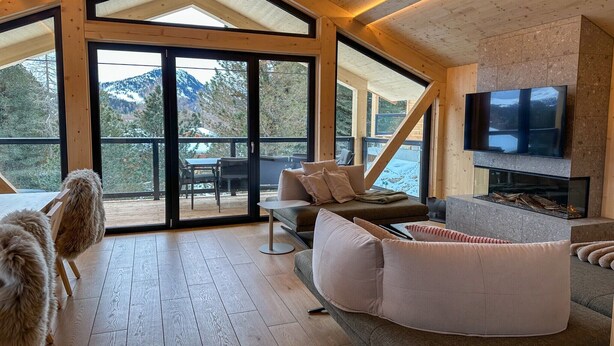 Un intérieur moderne avec un grand téléviseur, une cheminée et une vue sur les montagnes grâce à de grandes fenêtres.