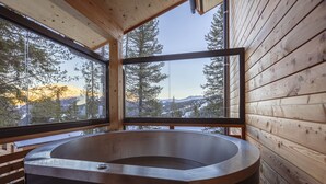 Une cabane en bois dotée d’une grande fenêtre en verre, d’une terrasse en bois et d’un bain à remous.