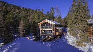 Une cabane en bois dotée d’un balcon, entourée de neige et d’arbres.