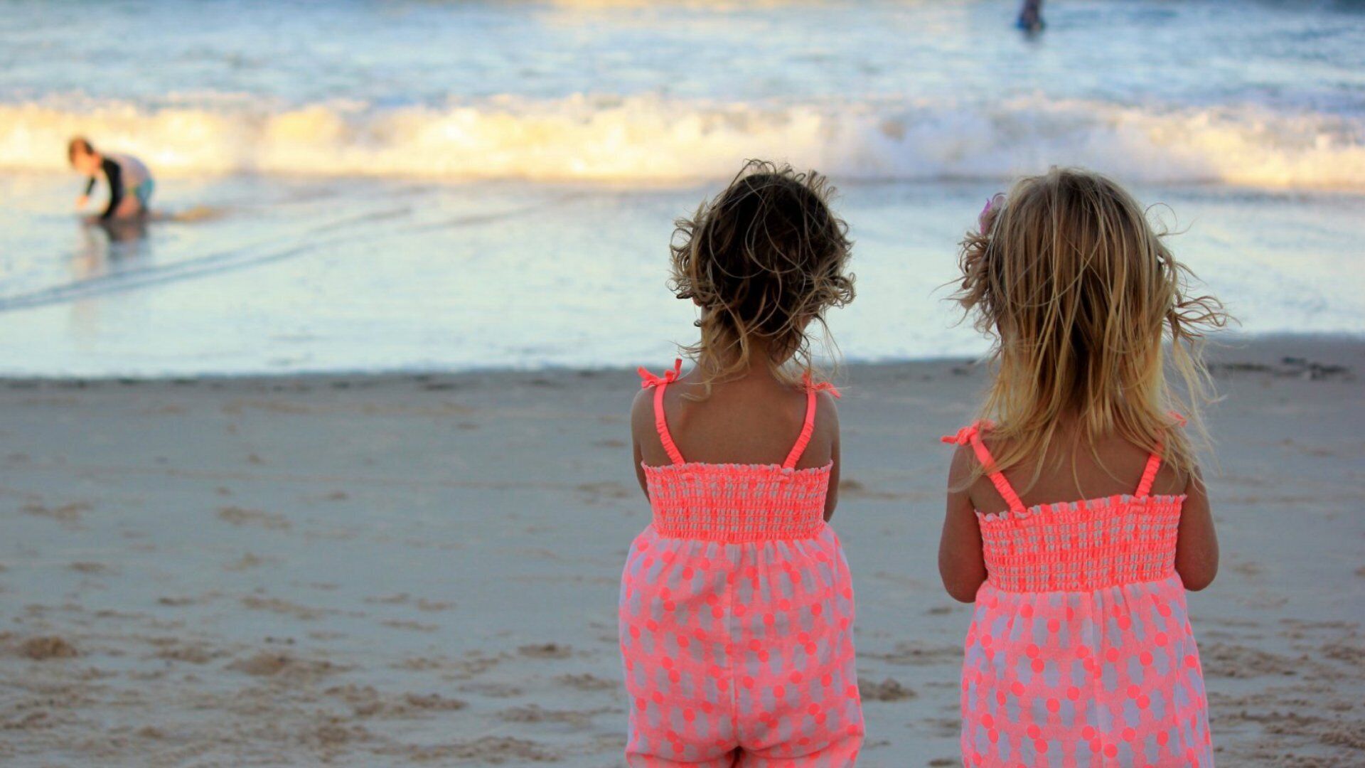 Two children standing on a sandy beach, facing the ocean.