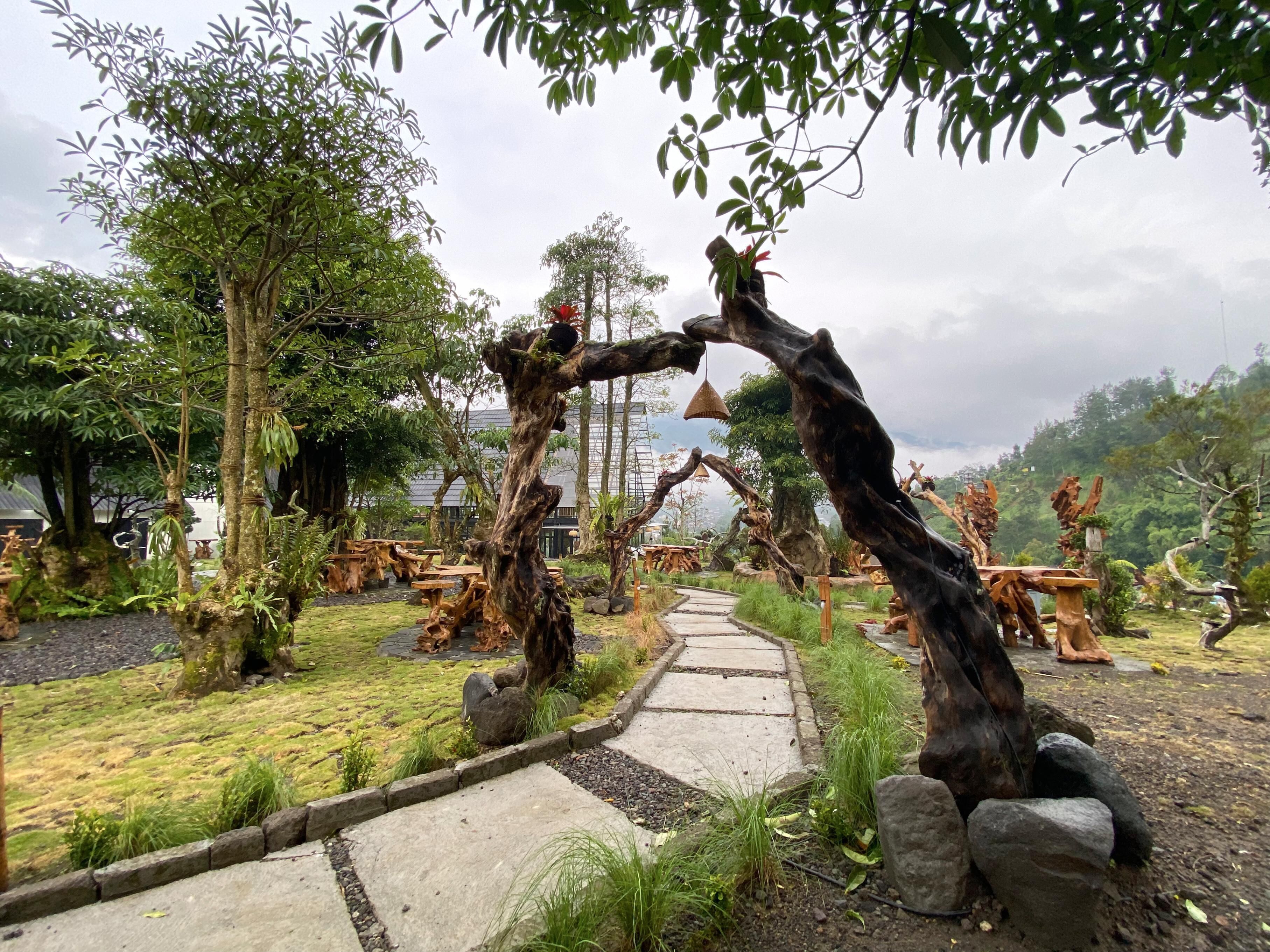 Un jardín con esculturas de madera únicas, un sendero de piedra y abundante vegetación.