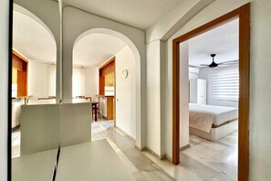 Une chambre d’hôtel avec un lit, un bureau et une chaise. Un couloir mène à une autre pièce.