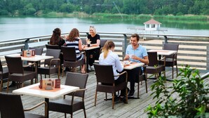 Un groupe de personnes est assis à une table dans un restaurant en plein air, avec des chaises, et profite de la vue sur un lac.
