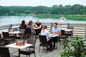 A group of people dining at an outdoor restaurant with tables and chairs, overlooking a lake.
