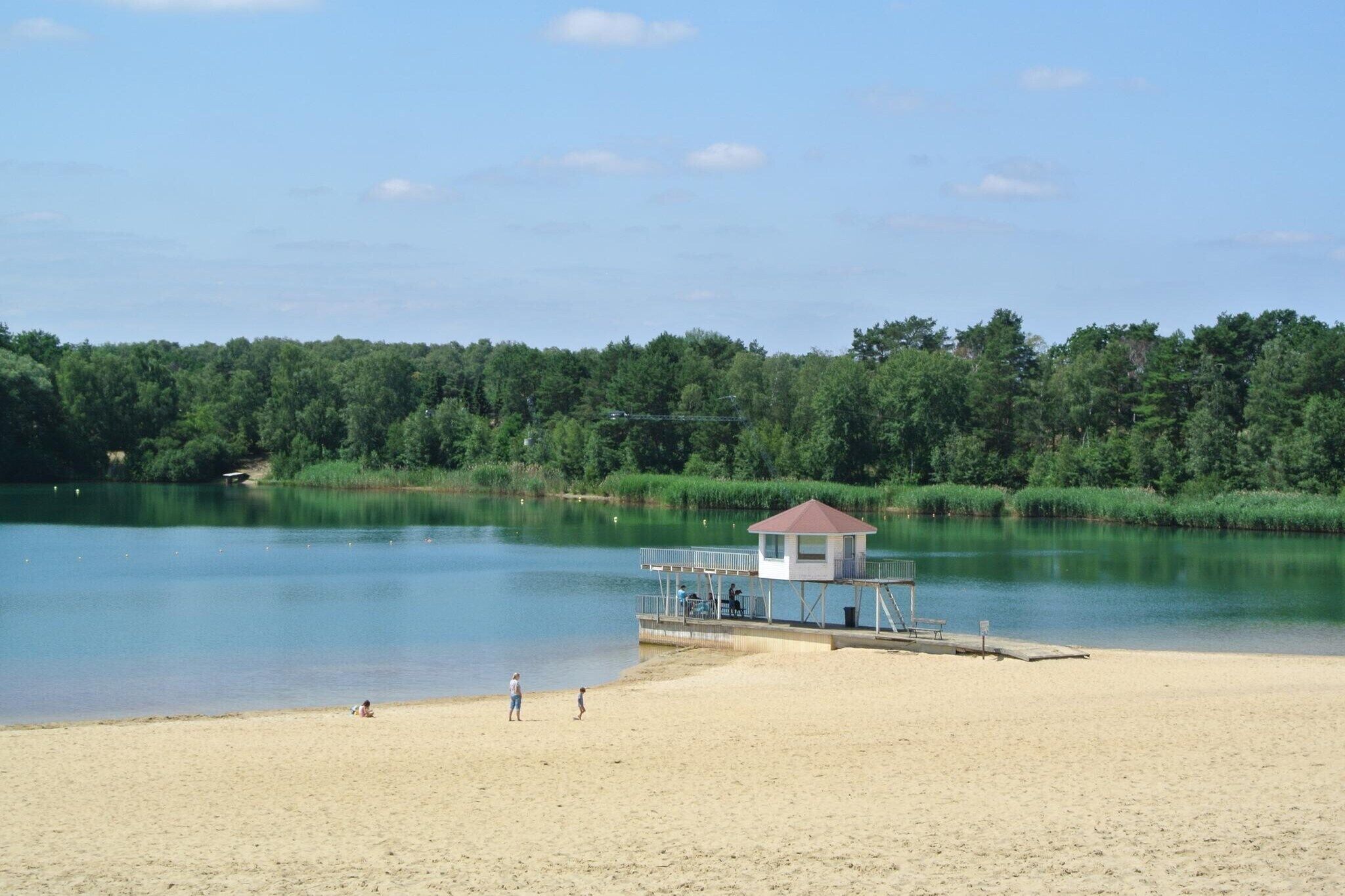 A beach with a lifeguard tower, sandy shore, calm water, and dense greenery in the background.
