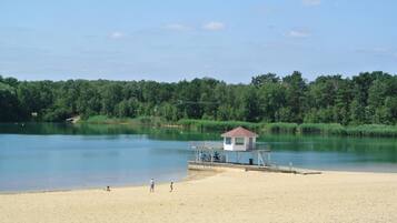 A beach with a lifeguard tower, sandy shore, calm water, and dense greenery in the background.