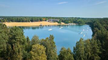 A lake surrounded by dense forest, with boats anchored in the water and a building with a beach in the background.