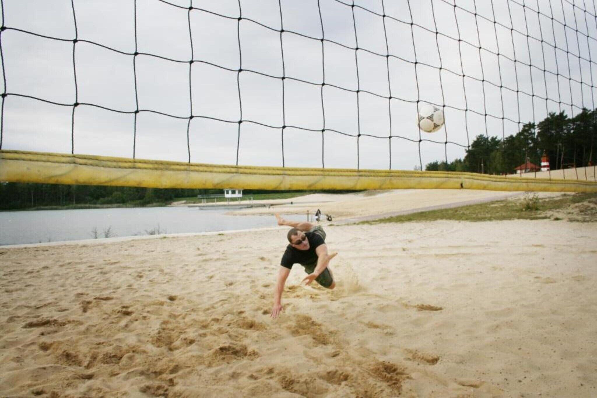 A volleyball net with a sandy court and a body of water in the background.
