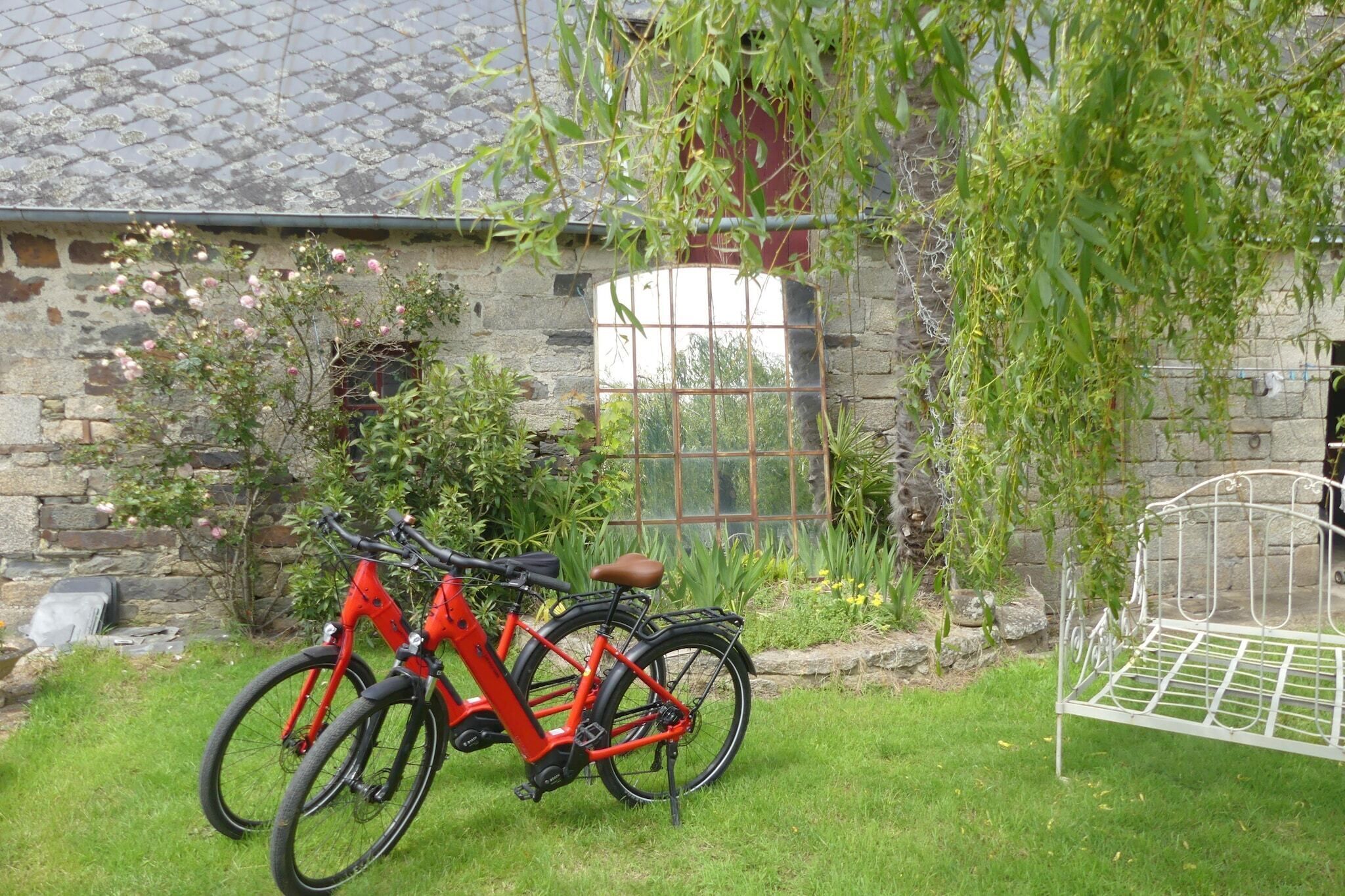 Un bâtiment en pierre avec un portail en métal, un vélo rouge et un banc en métal.