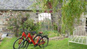 Un bâtiment en pierre avec un portail en métal, un vélo rouge et un banc en métal.