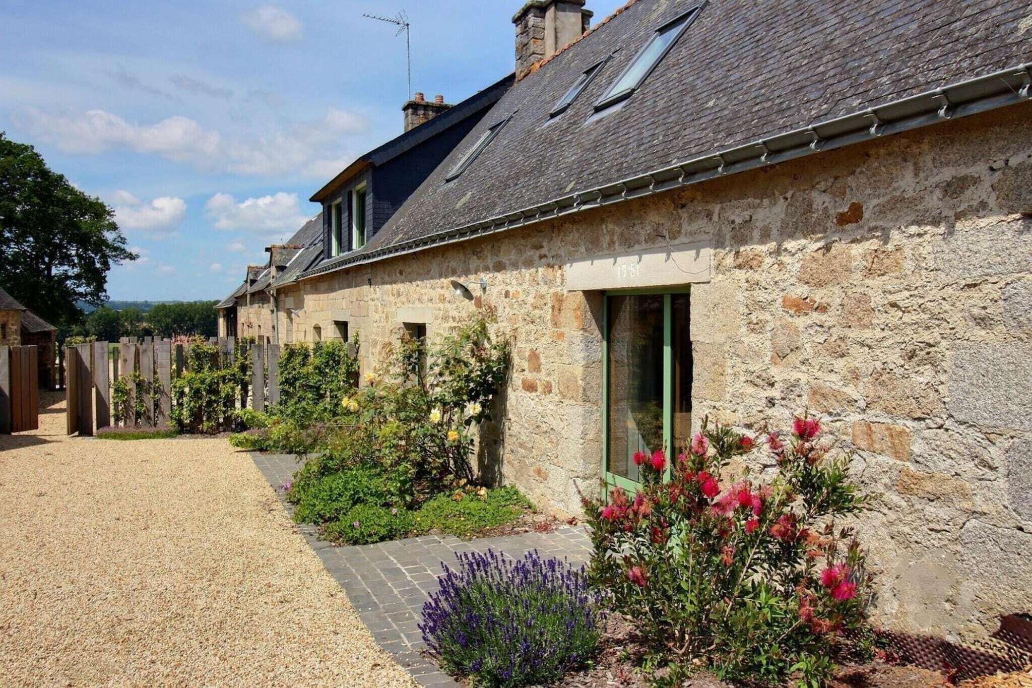 Un bâtiment en pierre avec une allée gravillonnée et un jardin agrémenté de fleurs et d’arbustes.