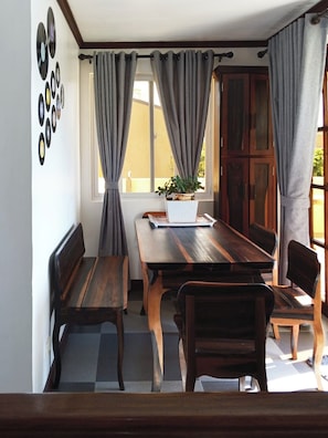 Ein Essbereich mit einem Holztisch, Bänken, einem Blumentopf und einem Fenster mit Vorhängen.
