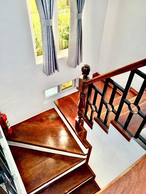 Eine Holztreppe mit schwarzer Geländer, ein Feuerlöscher auf der linken Seite und ein Fenster mit Vorhängen.