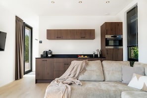 A modern kitchen with wooden cabinets, a built-in oven, and a black countertop. - Luxurious 4-person wellness villa on the Vogelenzang Estate with a private sauna. Bright, comfortable, and sustainably furnished, surrounded by greenery and close to the dunes and coast. (Vogelenzang)