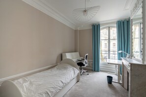 Ein Schlafzimmer mit einem Einzelbett, einem Schreibtisch, einem Stuhl und einem Fenster mit Vorhängen.