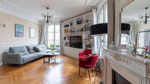 A living room with a sofa, a red chair, a fireplace, and a bookshelf. - Bright And Spacious 3BDR Apt Near Eiffel Tower (Paris)