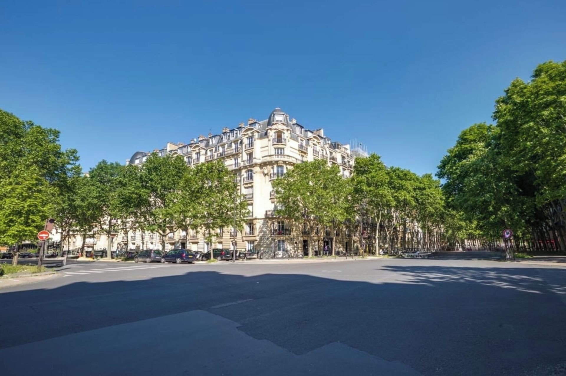 A large, historic building with classical architecture, surrounded by trees and a clear sky.