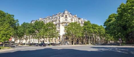 A large, historic building with classical architecture, surrounded by trees and a clear sky.