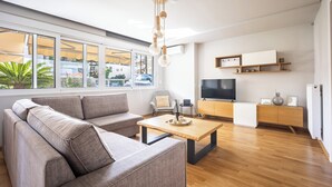 A modern living room with a sofa, coffee table, TV, and wooden flooring. - Athenean Riviera Posh Apartment-GF1 (Glifada)