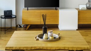 A modern living room with a wooden dining table, a flat-screen TV, and a hanging light fixture. - Athenean Riviera Posh Apartment-GF1 (Glifada)