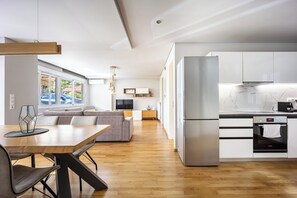 Una cocina moderna con electrodomésticos de acero inoxidable, un comedor con mesa de madera y una sala de estar con sofá y televisor.