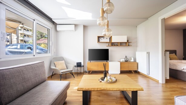 A modern living room with a sofa, a wooden coffee table, a TV, and a dining area. - Athenean Riviera Posh Apartment-GF1 (Glifada)