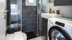 Uma casa de banho moderna com cabine de chuveiro em vidro, sanita, máquina de lavar roupa e lavatório.