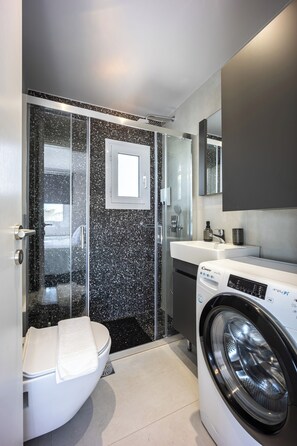 Ein modernes Badezimmer mit Duschkabine aus Glas, Toilette, Waschmaschine und Waschbecken.