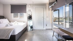 Quarto de hotel moderno com cama, um banco, uma janela grande e uma porta.
