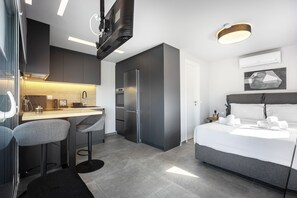Een moderne hotelkamer met een keukenhoek, een bed met witte lakens en een barkruk.
