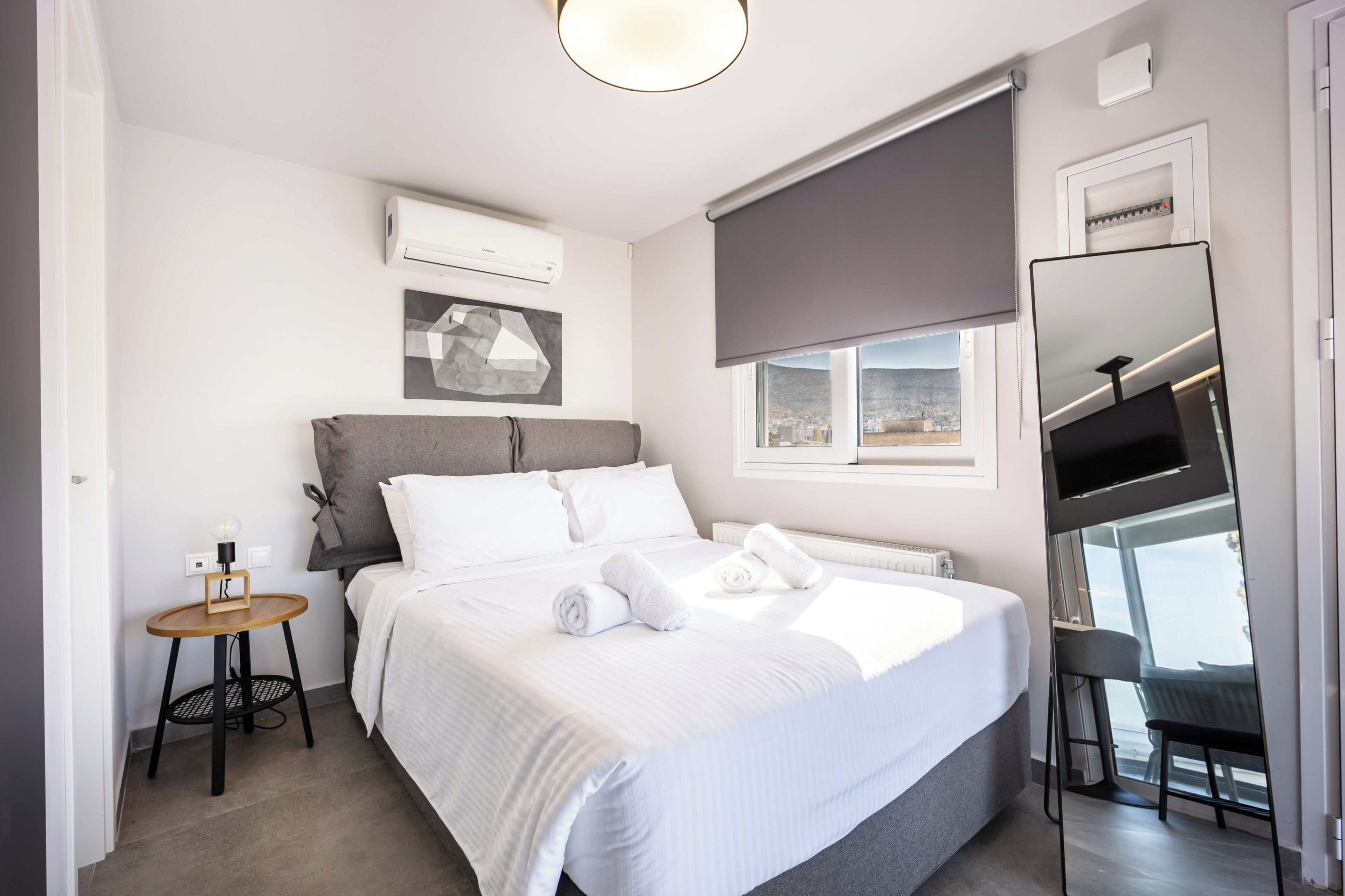 A hotel room with a bed, a small table, a TV, and a window with a view.
