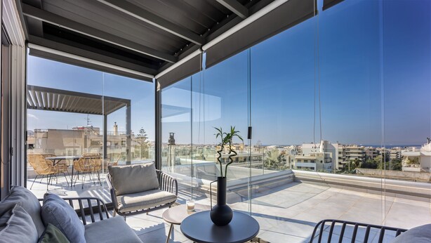 Um terraço moderno no telhado, com guarda-corpo de vidro, mobiliário para áreas externas e vista para a paisagem urbana.