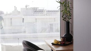 Quarto com uma janela grande, uma cadeira, uma mesa com alimentos e um vaso de planta.