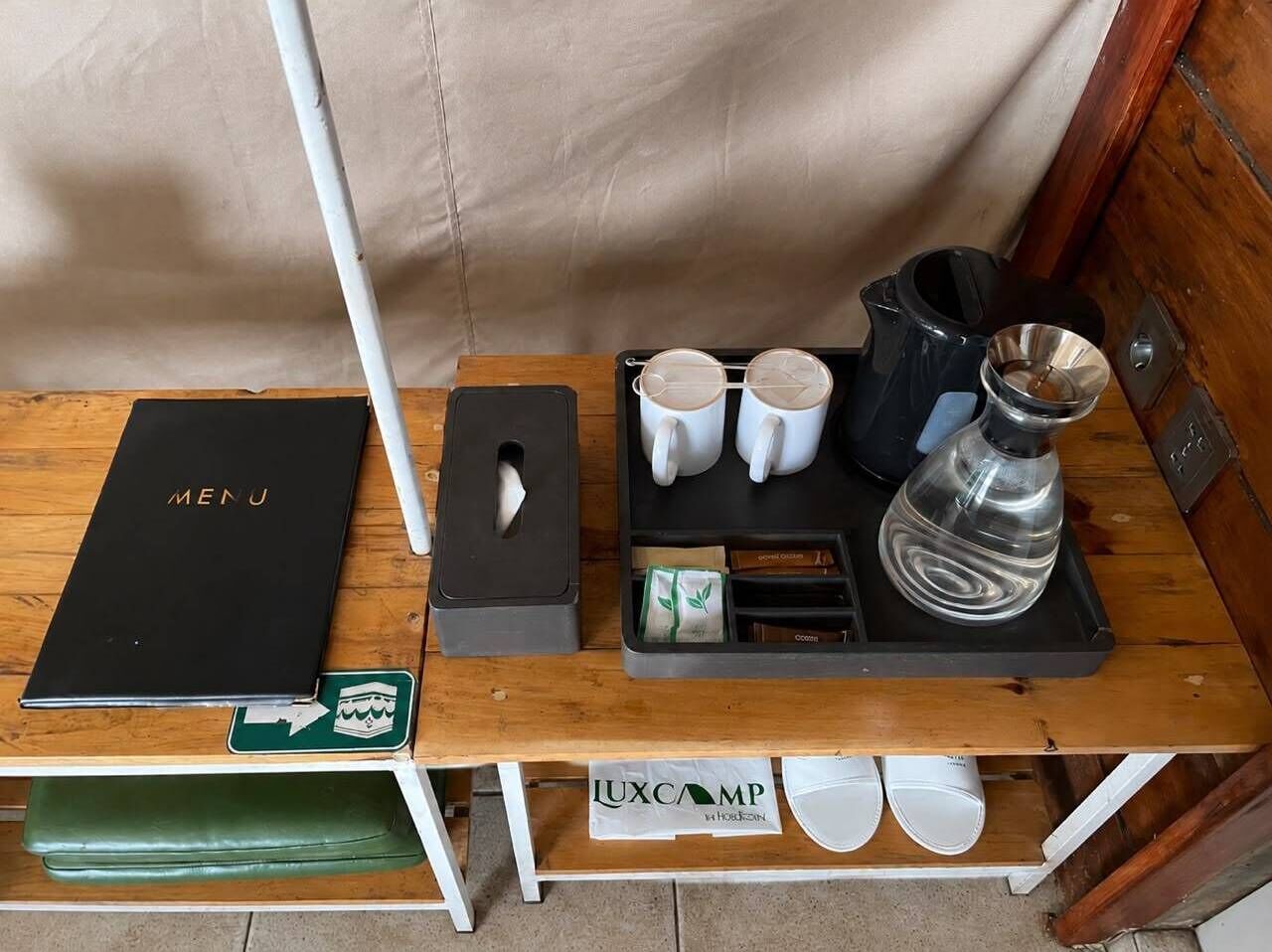 A wooden table with a black menu, a coffee maker, and a tray with cups and a teapot.