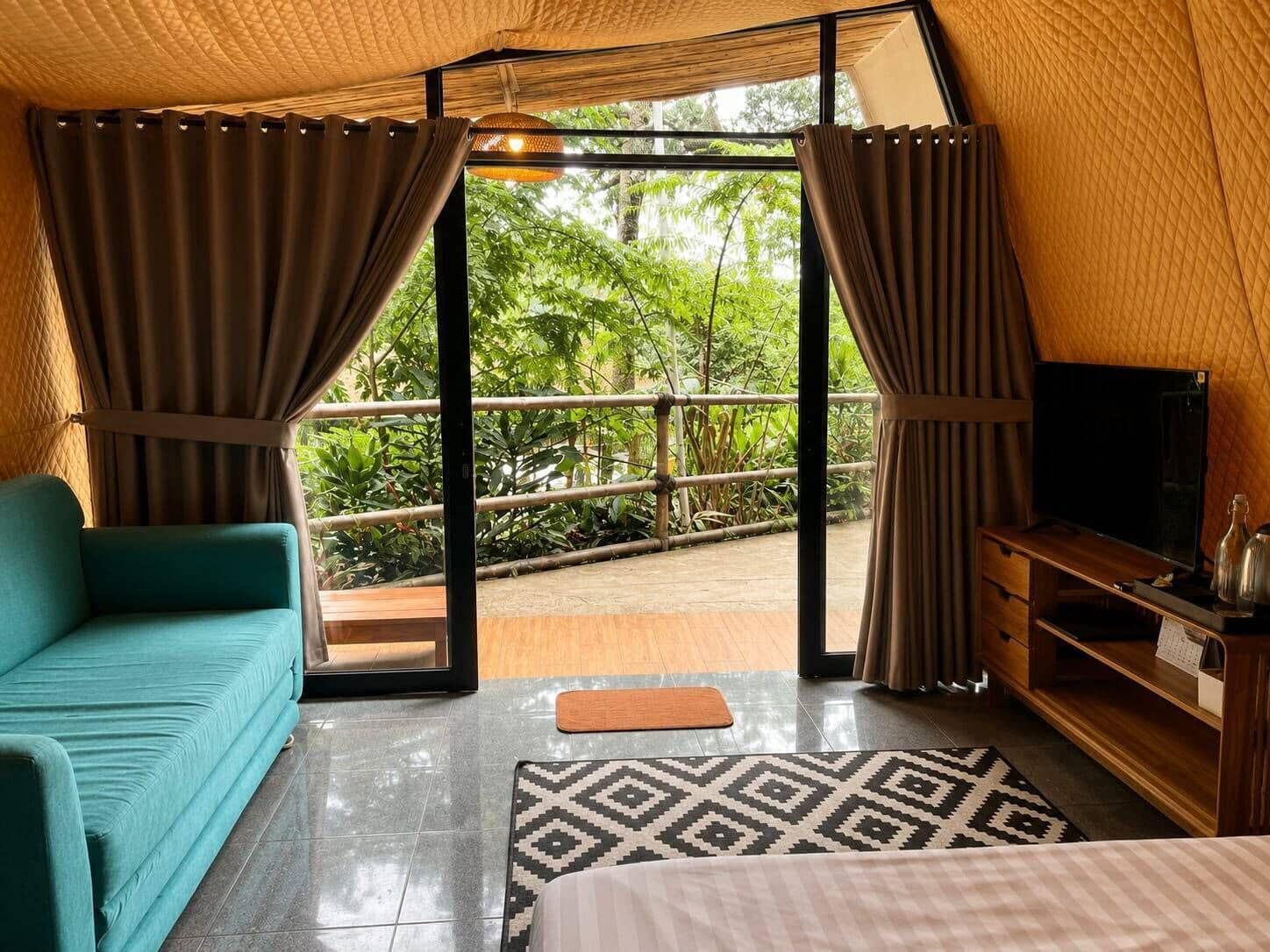 A room with a sofa, a TV, a wooden cabinet, and a view of greenery outside.