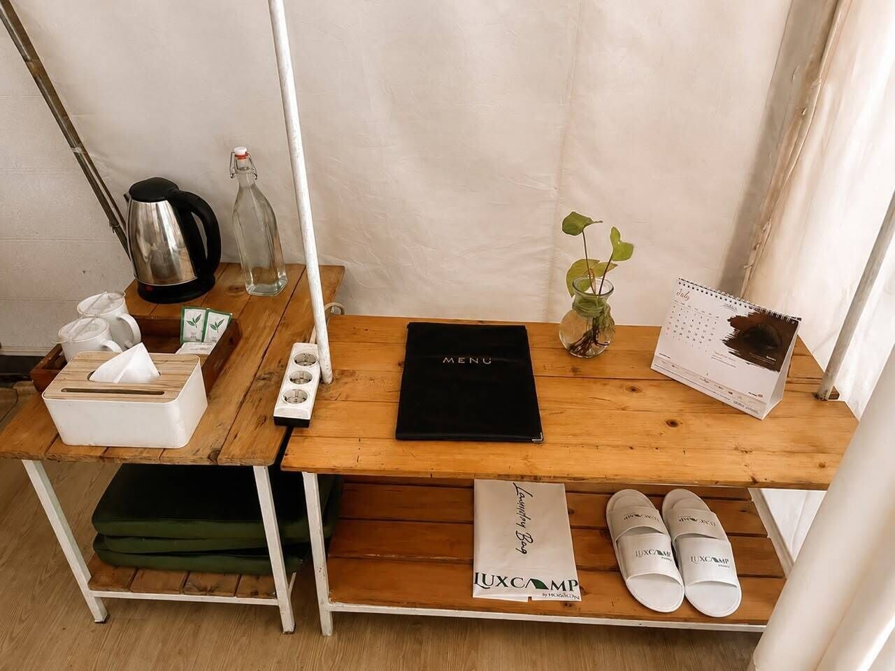 A wooden table with a black menu, a tissue box, a glass bottle, a plant, a calendar, and white slippers.