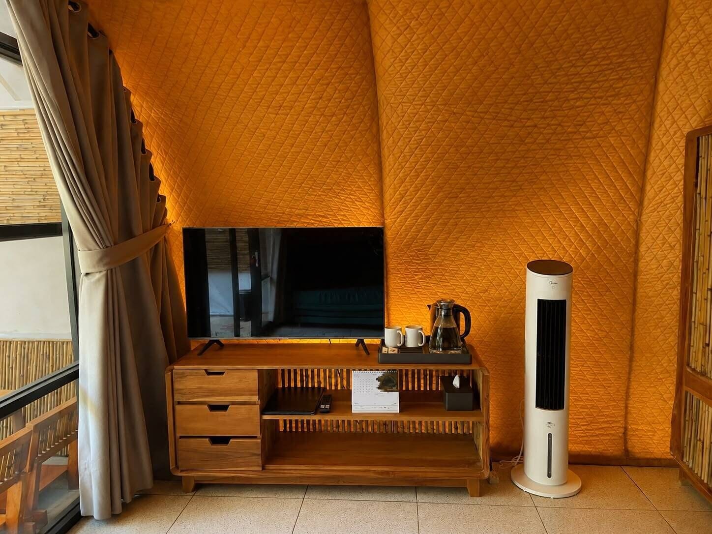 A room with a television on a wooden stand, a white air purifier, and a small table with a kettle and cups.