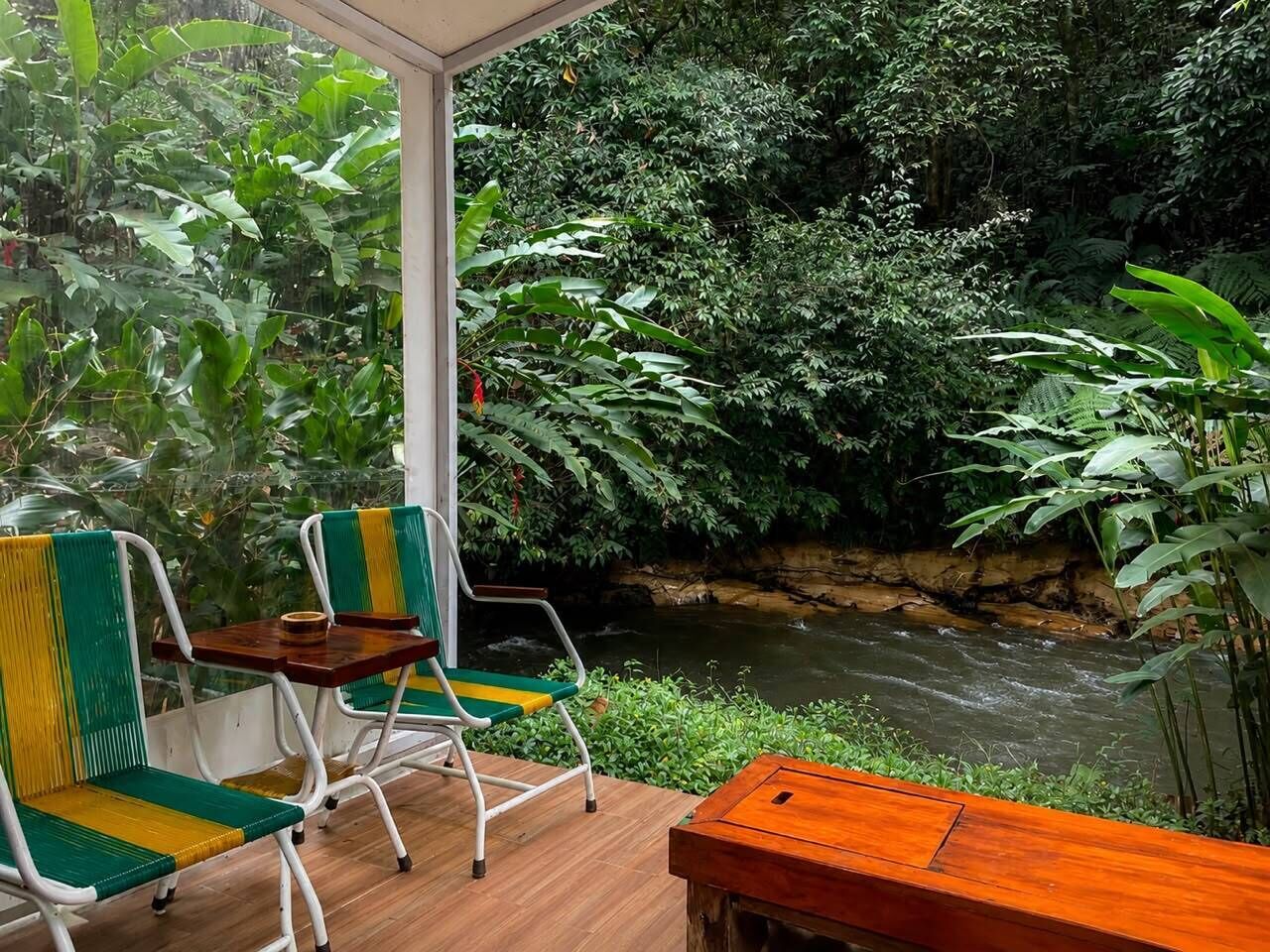 A wooden deck with two chairs and a table, overlooking a river and dense greenery.